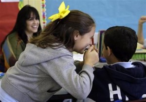 Duna López, de ocho años, le comenta algo al oído a su compañerito Mathew Botros, de nueve, en una clase de inglés de la escuela bilingüe Coral Way K-8 de Miami. A la izquierda aparece la maestra Juliai Puentes. En las escuelas de EEUU hay muchos niños que no hablan inglés o que necesitan perfeccionarlo y ese es uno de los grandes retos de la educación estadounidense. Foto del 3 de abril del 2013. (AP Photo/Lynne Sladky, File)