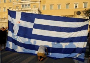 Un manifestante se arrodilla frente a la bandera de Grecia, durante una protesta anti-austeridad, en Atenas, Grecia, 29 de junio de 2015. Grecia intentó el martes un acercamiento de último minuto con sus acreedores internacionales en busca de ayuda, pero no fue suficiente para salvar al país de convertirse en la primer economía desarrollada en incumplir un préstamo con el Fondo Monetario Internacional. REUTERS/Yannis Behrakis