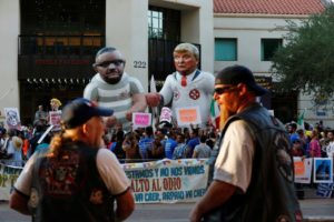 Men watch from across the street as protesters rally against Donald Trump, who is in town to speak on immigration, in Phoenix, Arizona. REUTERS/Nancy Wiechec